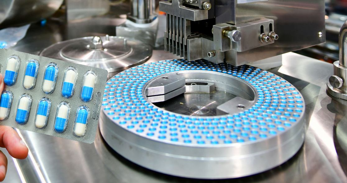 Hand holding blue capsule pack at medicine pill production line, Industrial pharmaceutical concept.banner side